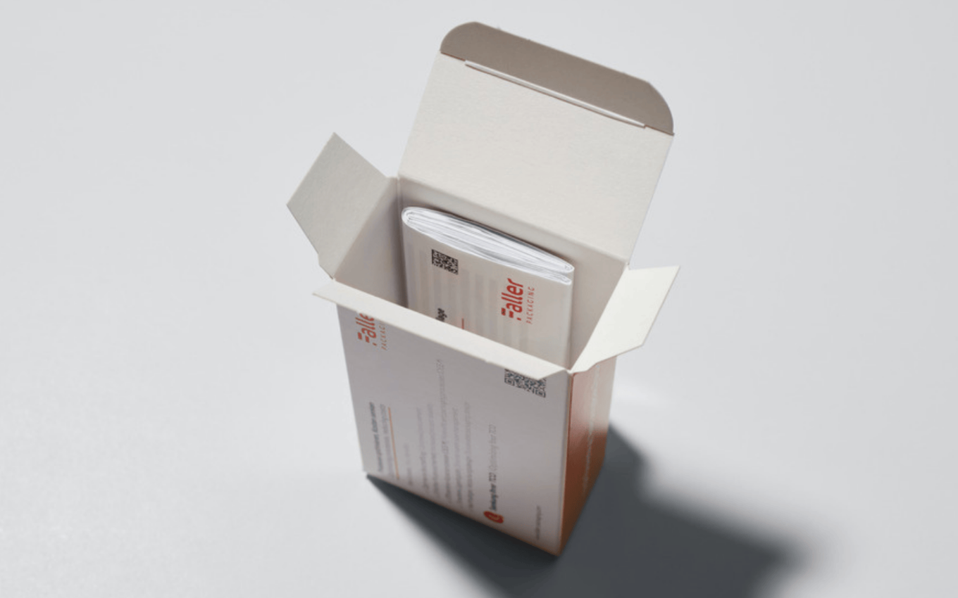 Geöffnete Faltschachtel mit integrierter Packungsbeilage für pharmazeutische Produkte zur Reduzierung von Verpackungsschritten.