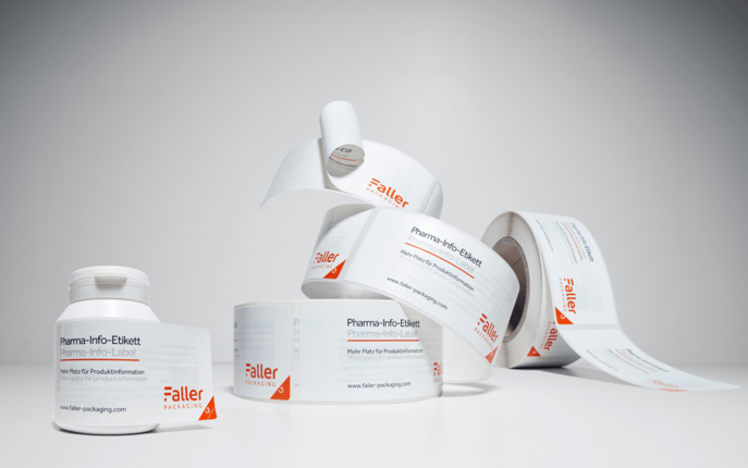 Gyógyszerinformációs öntapadós címkék hengerei, semleges háttérre elhelyezve. A címkék világosan fel vannak tüntetve, és a Faller márkát mutatják.
