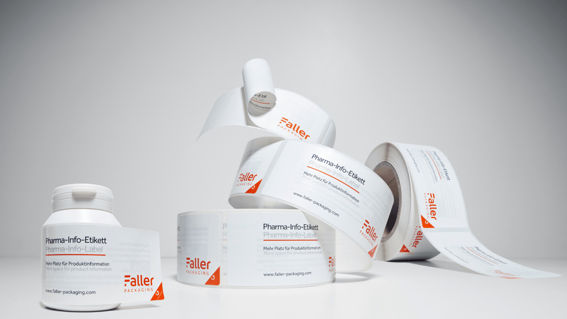 Gyógyszerinformációs öntapadós címkék hengerei, semleges háttérre elhelyezve. A címkék világosan fel vannak tüntetve, és a Faller márkát mutatják.