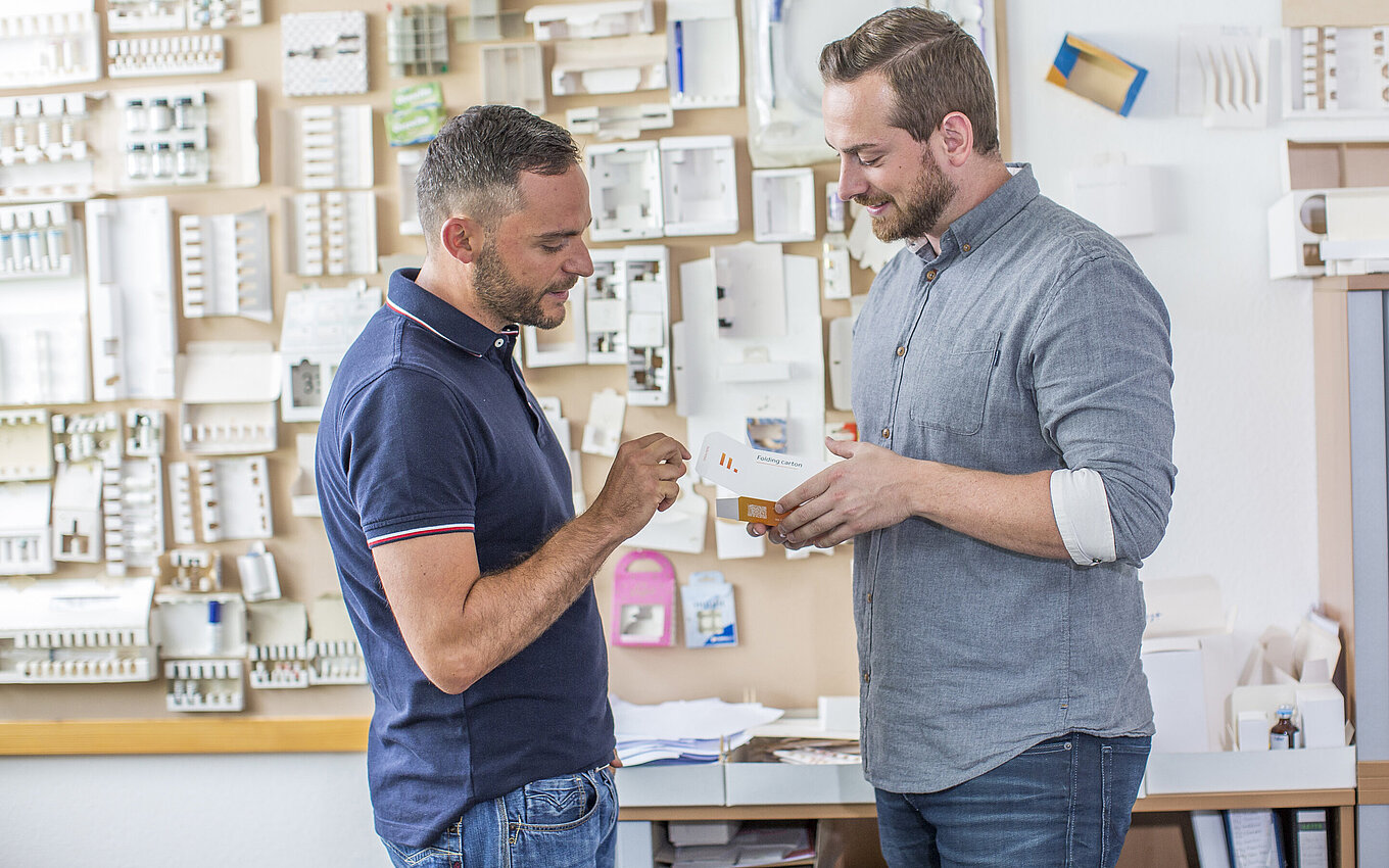 Development of innovative combination products at Faller Packaging: two experts examining a pharmaceutical folding carton with integrated package leaflet.